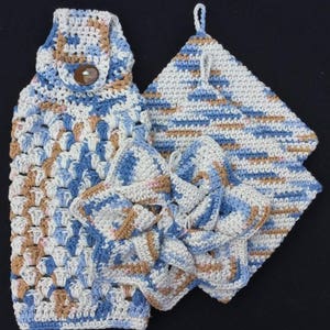 May include: Set of three crocheted kitchen towels in blue, brown, and white. The towels are made with a textured stitch and have a loop for hanging.