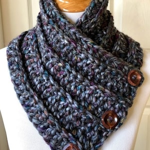 May include: A gray, multi-colored crocheted cowl with three wooden buttons. The cowl is folded over and the buttons are visible on the front.