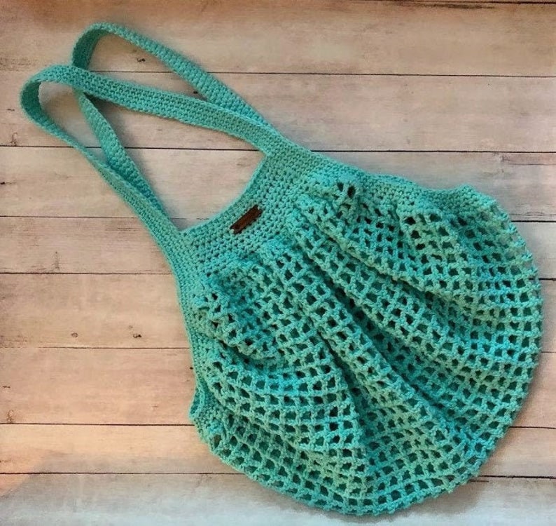 May include: A turquoise crocheted tote bag with a brown leather tag. The bag has a wide, open top and a mesh design.