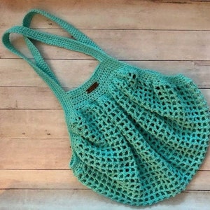May include: A turquoise crocheted tote bag with a brown leather tag. The bag has a wide, open top and a mesh design.