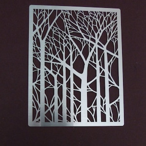 May include: A metal stencil featuring a design of bare trees with branches. The stencil is silver and has a rectangular shape.