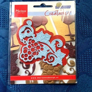 May include: A package of Marianne Design die cuts featuring a light blue grape vine design over a red background. The package includes other wine-themed die cuts. The text "Creatables" and "www.mariannedesign.nl" are visible.