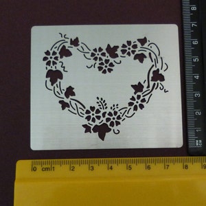 May include: A metal stencil with a heart-shaped design made of vines and flowers. The stencil is approximately 7.5 inches wide and 6 inches tall.