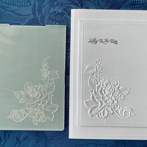 Peut inclure: Un dossier de gaufrage rectangulaire en plastique translucide avec un motif floral et une carte blanche assortie présentant le même motif floral en relief avec le texte noir imprimé Today Is The Day centré en haut de la carte.
