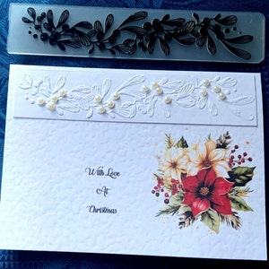May include: A white card with a red and white poinsettia flower design and the text "With Love At Christmas". The card has a white embossed border with pearl-like embellishments.