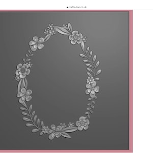 May include: A gray oval-shaped embossing folder featuring a raised floral wreath design. The wreath is composed of various five-petaled flowers, small buds, and elongated leaves arranged in a continuous loop against a smooth, dark gray background.