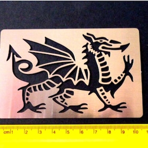 May include: A metal stencil of a black dragon with wings outstretched. The stencil is approximately 18 cm wide.