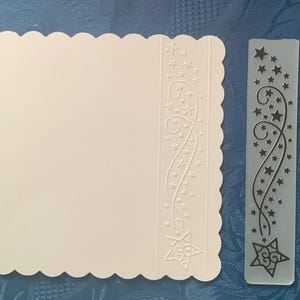 May include: A white card with a scalloped edge and embossed star design. A clear plastic template with a star and swirl design is next to the card. A ruler is also in the image.