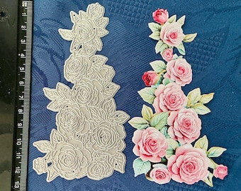May include: Two floral die cuts. One is a silver-colored metal die cut of roses and leaves. The other is a colorful arrangement of pink roses, red buds, and green leaves. The background is a dark blue fabric.