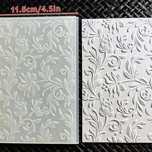 May include: A rectangular plastic embossing folder featuring a raised floral and vine pattern. The tool measures 4.5 inches by 6.3 inches. Beside it is a white cardstock sheet showing the embossed impression of the same intricate botanical design.