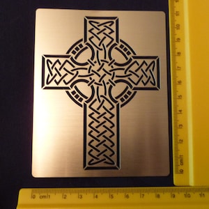 May include: A gold metal Celtic cross with intricate knotwork design. The cross is approximately 18 cm wide and 18 cm tall.