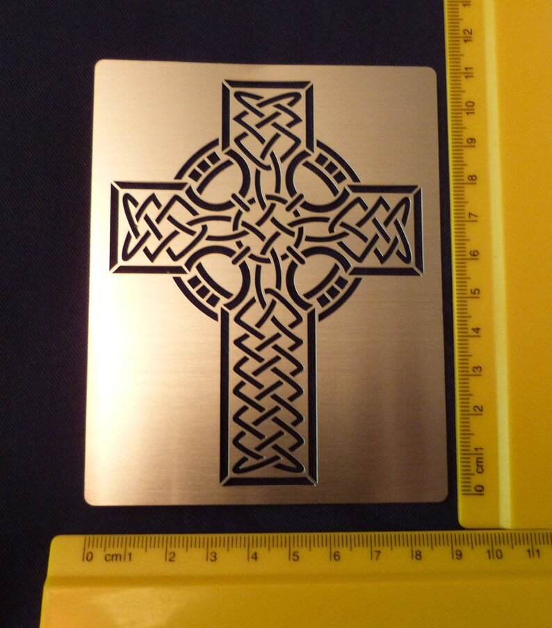 May include: A gold metal Celtic cross with intricate knotwork design. The cross is approximately 18 cm wide and 18 cm tall.