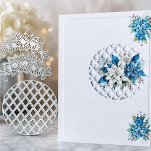 May include: A white greeting card featuring a circular lattice cutout layered over a blue and white poinsettia floral illustration, with matching floral accents in the corners. Beside it are two silver metal cutting dies of the same designs.