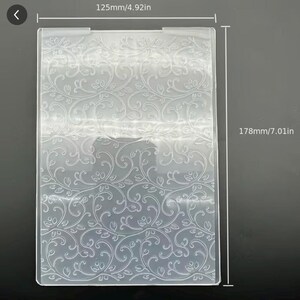 May include: A clear rectangular plastic embossing folder featuring an intricate embossed vine and leaf pattern. The folder measures 4.92 inches in width and 7.01 inches in height, with visible dimension lines and text indicating these measurements.