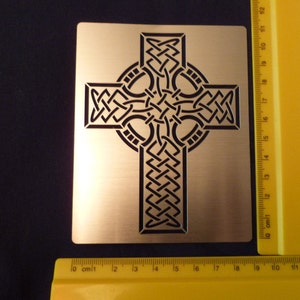 May include: A gold metal Celtic cross stencil with a black intricate knot design. The stencil is approximately 10 inches wide and 10 inches tall.