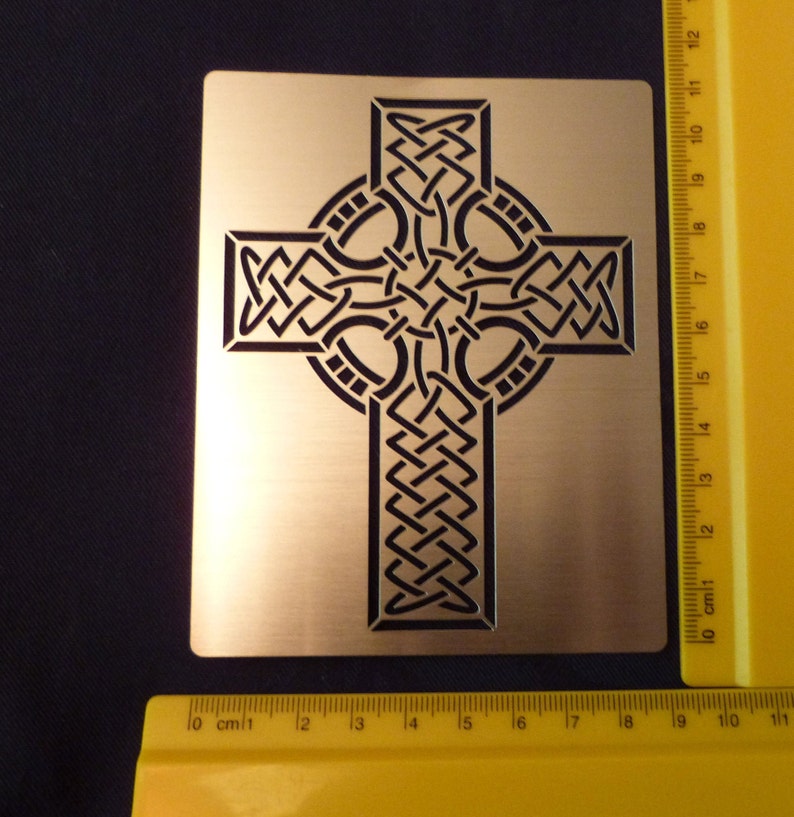 May include: A gold metal Celtic cross stencil with a black intricate knot design. The stencil is approximately 10 inches wide and 10 inches tall.