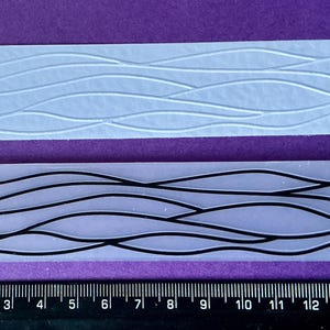 May include: Two rectangular silicone moulds with wave patterns. One has raised wave lines, the other has black wave lines. A ruler with centimetre markings is at the bottom, showing the moulds are approximately 15 cm long.