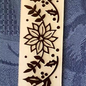 May include: A white polymer stamp with a black floral design featuring poinsettia and holly motifs. The stamp is approximately 7.6 cm tall.