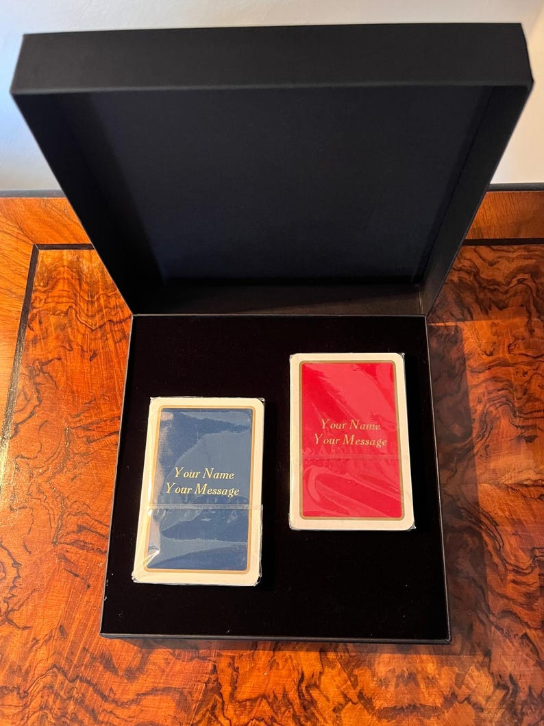 Op de afbeelding: Twee decks speelkaarten in een zwarte doos. De kaarten zijn gepersonaliseerd met de tekst "Your Name Your Message". Een deck is blauw en het andere is rood.