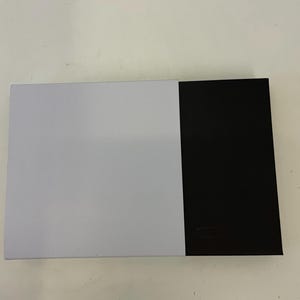 Op de afbeelding: Een witte en zwarte doos met een glad oppervlak. De doos is gesloten.