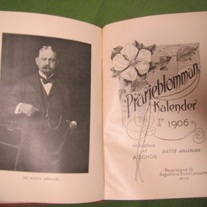 May include: A vintage book cover with a black and white photo of a man in a suit and tie. The cover also features a floral design with the text "Prarieblomman Kalender for 1906" and "Redigerad af A Sch"on Sj"atte Arg"angen".