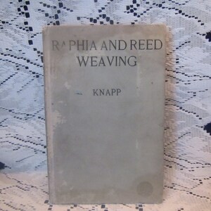 May include: A vintage book titled "RAPHIA AND REED WEAVING" by KNAPP. The book cover is a light gray color with black text.