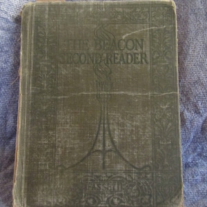 May include: A vintage green book with the title "The Beacon Second Reader" printed on the cover. The cover has a decorative design with a stylized torch.