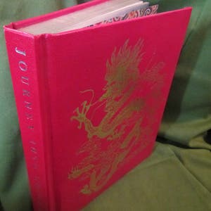 May include: A red hardcover book with the title "Journey to the West" printed in gold lettering on the spine. The front cover features a gold embossed illustration of a dragon.