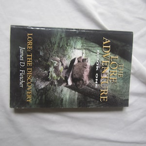 May include: The Lore of Adventure book cover, book one, titled "Lore: The Discovery" by James D. Fletcher. The cover features a dark green and black background with a shadowy figure in the center.