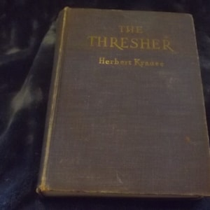 May include: A dark blue hardcover book with gold lettering on the spine. The title is "THE THRESHER" by Herbert Krause.