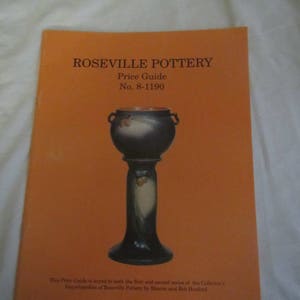 May include: A price guide for Roseville Pottery, featuring a blue and white ceramic planter with acorn accents on a stand. The guide is keyed to the first and second series of the Collector's Encyclopedias of Roseville Pottery by Sharon and Bob Haxford.  No. 8-1190.