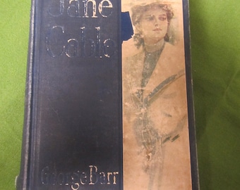 May include: A vintage hardcover book titled "Jane Cable" by George Barr McCutcheon. The book cover features a black and white illustration of a woman in a hat and coat.