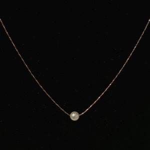 May include: A delicate gold chain necklace with a single white pearl pendant.