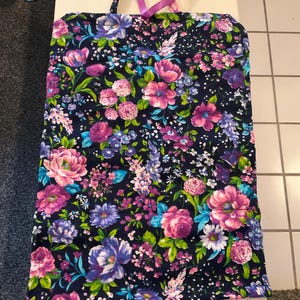 May include: A floral tote bag with a dark navy background and a vibrant pattern of pink, purple, and blue flowers. The bag has a rectangular shape with a handle and a pink ribbon. The bag is made of fabric.