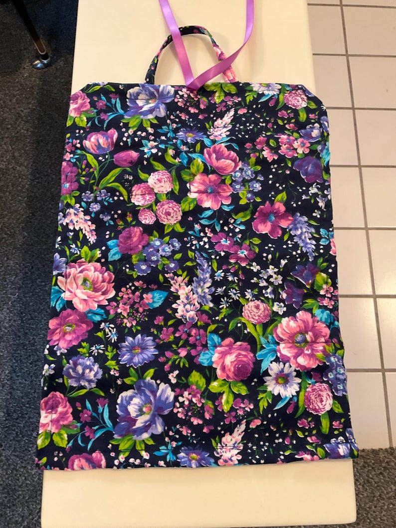 May include: A floral tote bag with a dark navy background and a vibrant pattern of pink, purple, and blue flowers. The bag has a rectangular shape with a handle and a pink ribbon. The bag is made of fabric.
