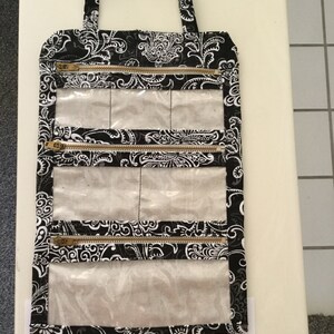 May include: Black and white paisley print jewelry travel case with a handle. The mini case has four zippered compartments with clear plastic windows. The case measures 8" x 12".
