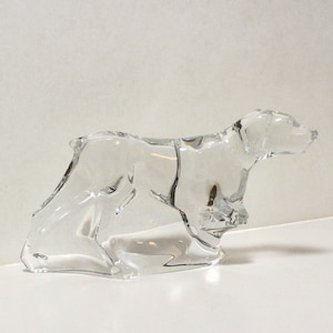 May include: A clear glass sculpture of a dog in a running pose. The sculpture is detailed and realistic, capturing the dog's movement and form.