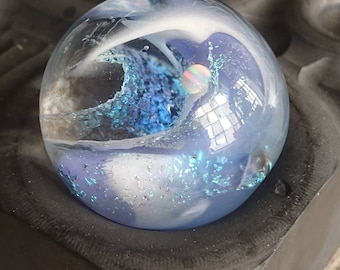 May include: A clear glass orb with a swirling blue and white design. The orb has iridescent glitter embedded in the glass.