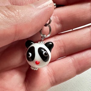 May include: A black and white glass panda charm with red nose and black eyes. The charm is attached to a silver chain.