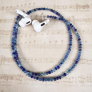 May include: A blue and white beaded chain with two white earbud holders. The chain is made of small glass beads in shades of blue and white.
