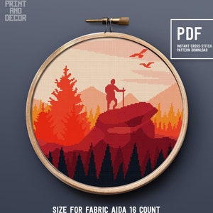 Puede incluir: Un patrón de punto de cruz que presenta a un excursionista de pie sobre una roca con un bosque y montañas en el fondo. El patrón está en un esquema de color rojo, naranja y amarillo. El patrón es para tela Aida de 16 hilos y mide 22,07 cm por 22,07 cm. El patrón está disponible como descarga instantánea en PDF.
