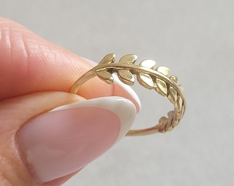 May include: A gold-colored ring featuring a delicate leaf design. The ring's band is thin, and the leaves are intricately detailed. The ring is held against a soft, neutral background, highlighting its elegant simplicity. A piece of jewelry.