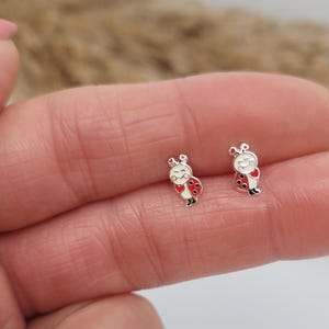 May include: A pair of silver ladybug earrings with red and white enamel. The ladybugs have black eyes and a smiling face.
