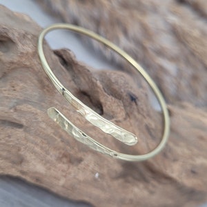May include: A gold hammered bangle bracelet with a unique open design. The bracelet is made of a single piece of metal that is bent into a circle and then hammered to create a textured surface.