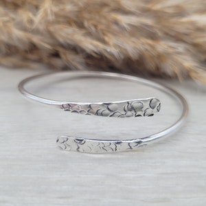 Może przedstawiać: Srebrna bransoletka typu bangle z fakturą młotkową. Bransoletka jest otwarta i ma prosty design.