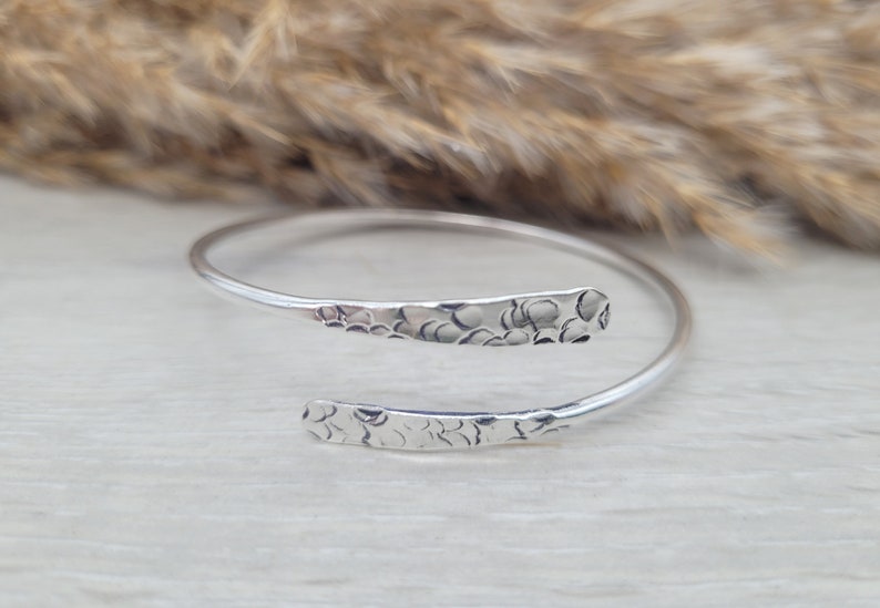 Może przedstawiać: Srebrna bransoletka typu bangle z fakturą młotkową. Bransoletka jest otwarta i ma prosty design.