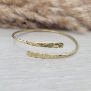 May include: A gold hammered metal bangle bracelet with a simple, open design.