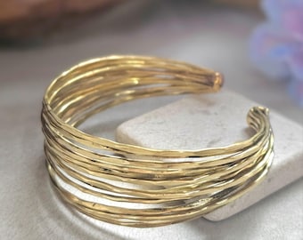 May include: A gold-colored cuff bracelet with a textured, layered design. The bracelet is made of multiple strands of metal, creating a bold and stylish accessory. The open design allows for easy wear. A statement piece for any jewelry collection.