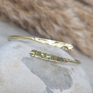 May include: A gold hammered metal bangle bracelet with a simple, minimalist design.