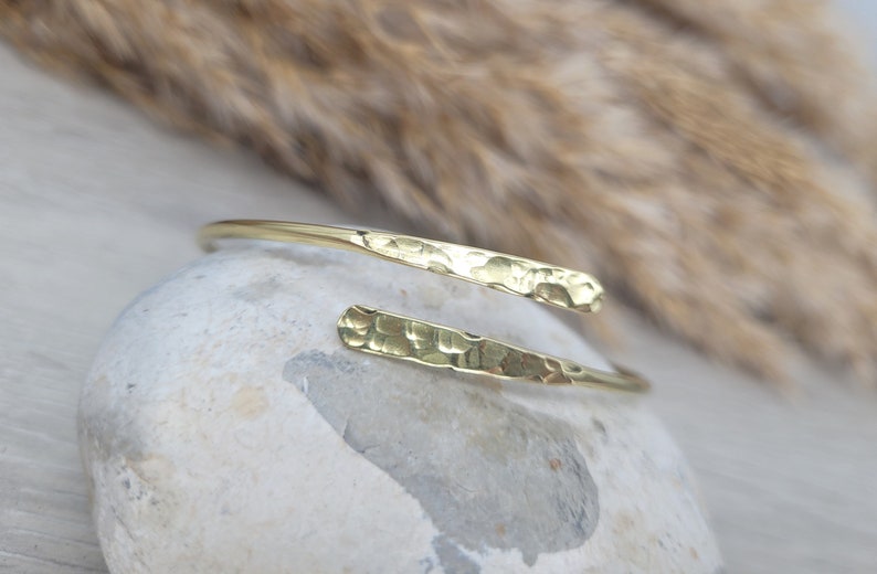 May include: A gold hammered metal bangle bracelet with a simple, minimalist design.
